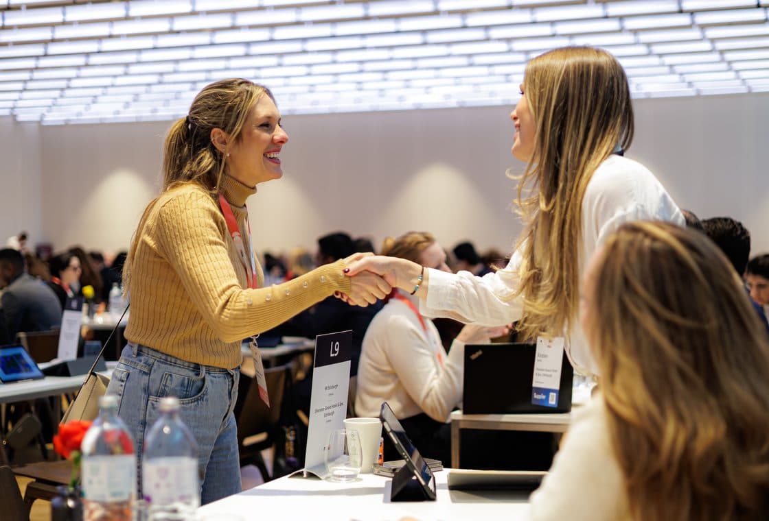 Two delegates shaking hands across a meeting table at an M&I event
