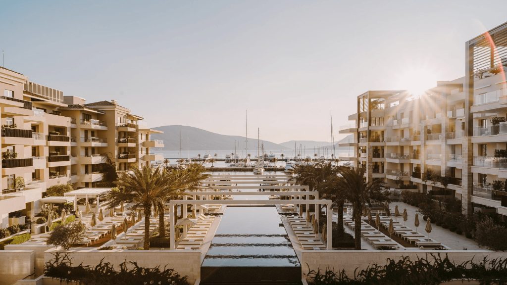 A picture of a luxurious sea view, with a hotel, water feature and trees.